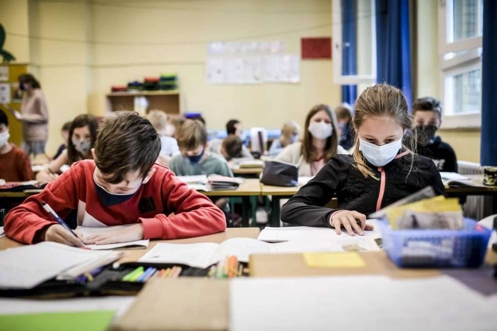 Revolution der Bildung – Kinder sitzen in einem modernen Klassenzimmer mit Masken
