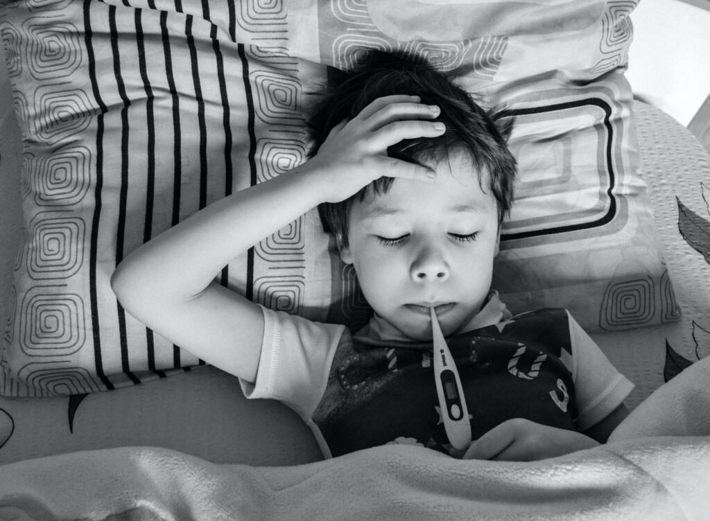 Ein krankes Kind liegt im Bett mit einem Fieberthermometer – Symbol für frühe Signale, wie dein Körper mit dir spricht