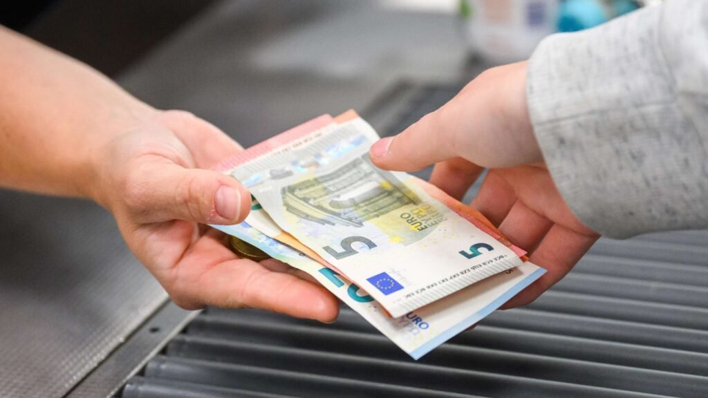 Hände übergeben Euro-Banknoten an einer Supermarktkasse – Abschaffung des Bargelds bedroht diesen Vorgang