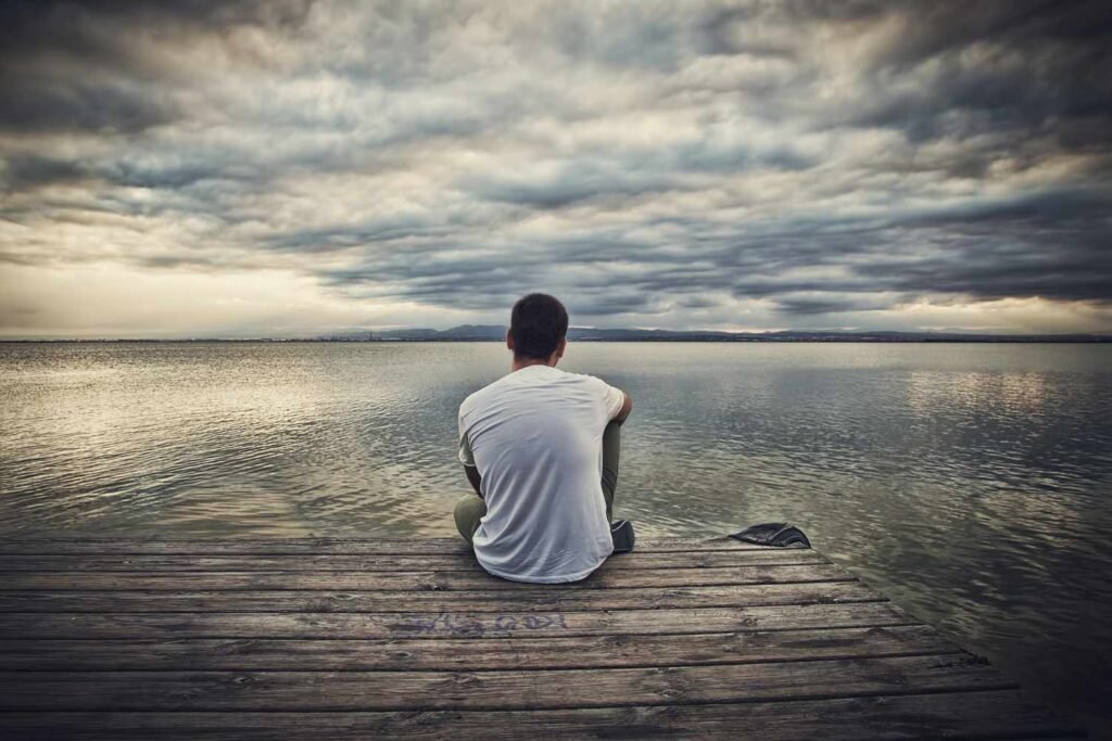 Ein Mann sitzt allein am Steg vor einem stillen See und blickt in die Ferne – Symbol für das stille Leben ehrlicher Einzelgänger