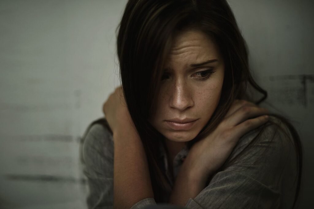 Eine junge Frau mit ängstlichem Blick sitzt zusammengerollt – visuelle Darstellung der emotionalen Probleme durch Angst.