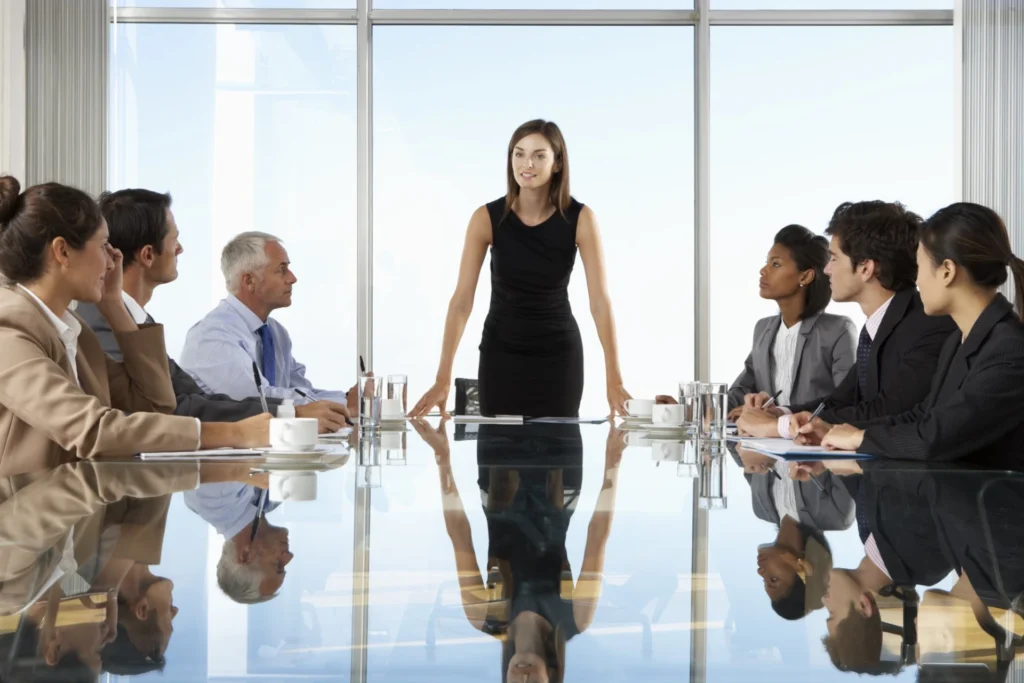 Frau steht im Meeting vor einem Team und zeigt durchsetzungsstarken Fokus im Business-Kontext