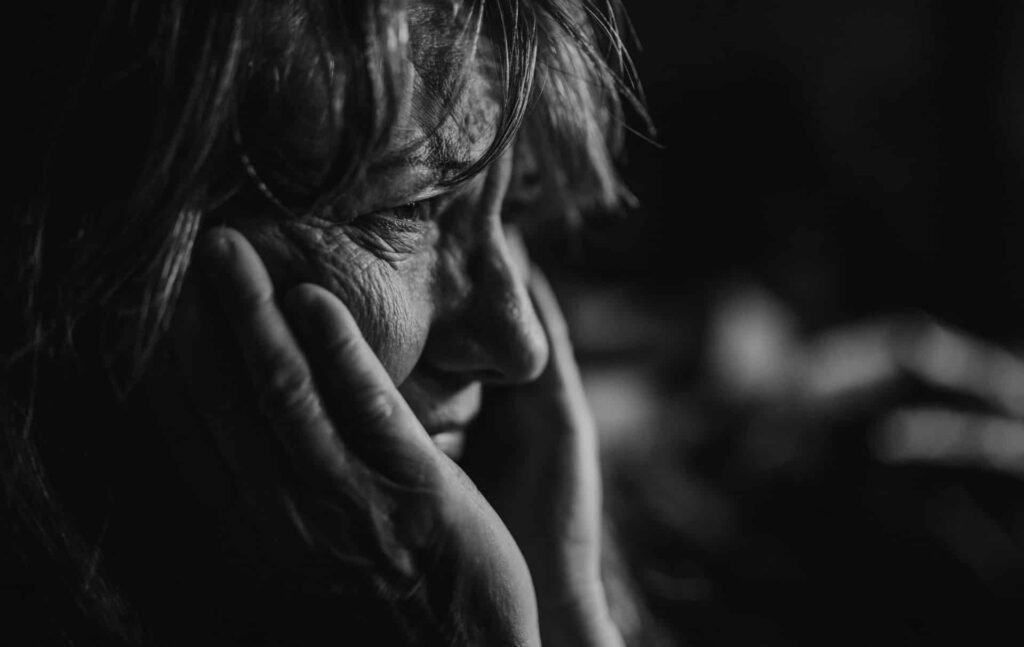 Eine ältere Frau hält sich das Gesicht – Zivilisation als Wahnsinn in Nahaufnahme