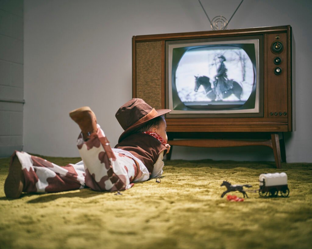 Kind im Cowboykostüm schaut gebannt in alten Fernseher – Darstellung der Realitätsverzerrung durch Fernsehen in jungen Jahren