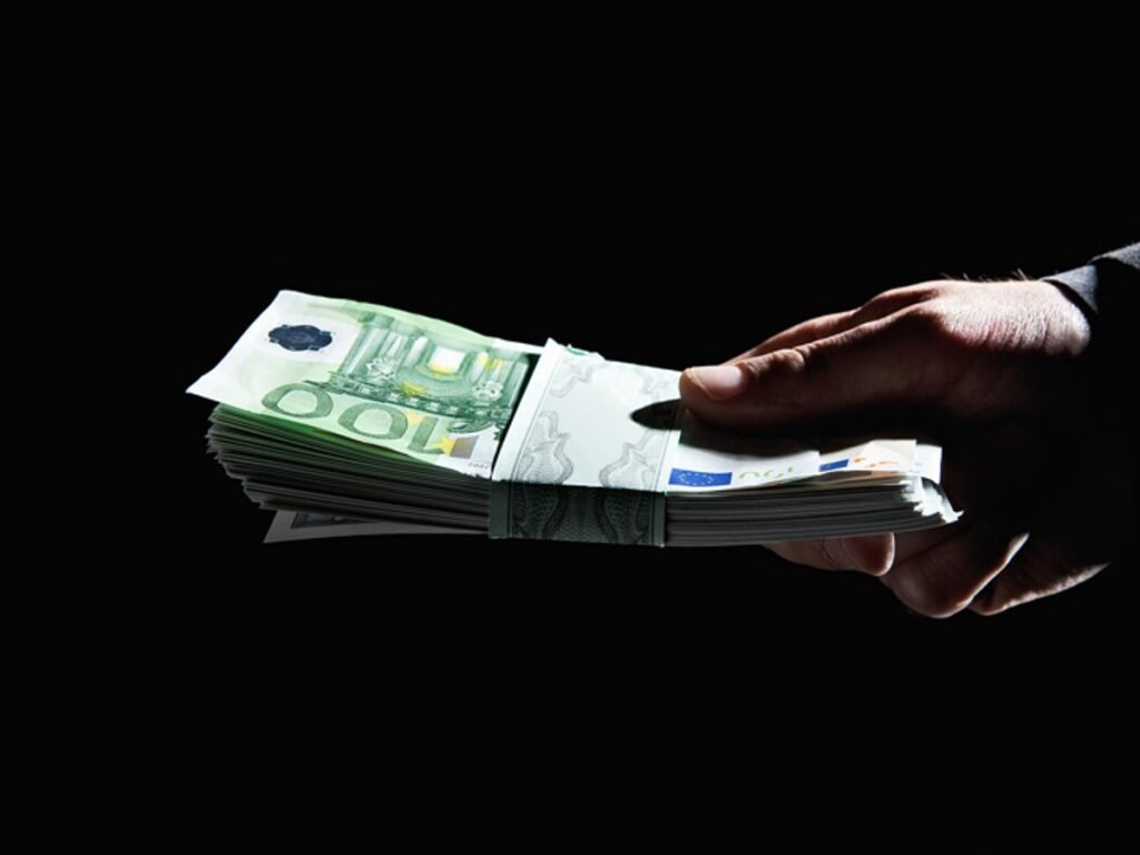 Hand überreicht ein Bündel 100-Euro-Scheine im Dunkeln – Diskussion um Abschaffung des Bargelds und Anonymität