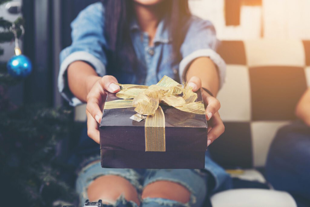 Frau überreicht Geschenk mit goldener Schleife – Symbolbild für Mitleid oder Egoismus
