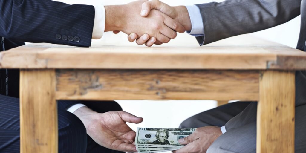 Zwei Männer geben sich die Hand über dem Tisch, während darunter Geldscheine überreicht werden – Symbol für Lobbyismus & Korruption