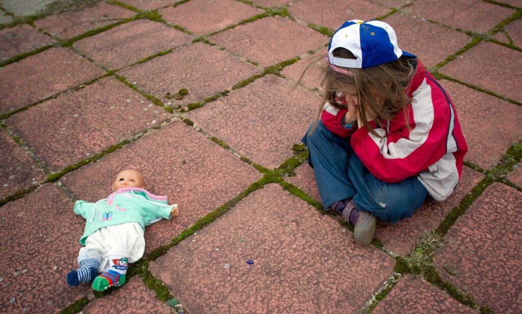 Ein Kind sitzt weinend neben einer Babypuppe – Sinnbild für emotionale Vernachlässigung durch unvorbereitete Elternschaft